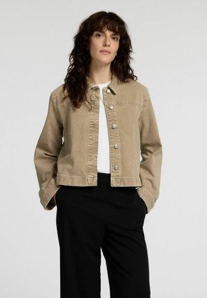 Beige denimjacka med krage, framknäppning med tryckknappar och lång ärm. Bärs över en vit topp och svarta byxor.