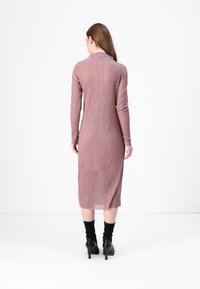 Ilga, susipjaustyta suknelė mauve spalvos, su ilgu rankovėmis ir prigludusia siluetu. Iki vidurio blauzdų ilgio, su subtiliu įpjovimu gale.