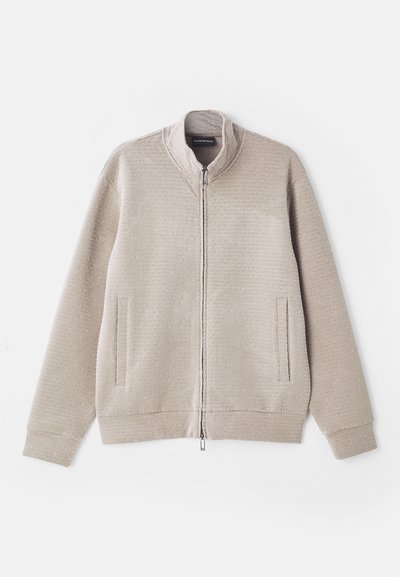 béžová prešívaná bunda na zips s textúrovanou látkou, stojatým golierom a dvoma prednými vreckami. Má jemný vzor a pletené manžety.