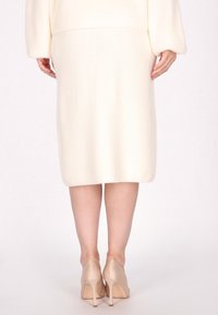 Knie-lange, ribbelige, witte gebreide rok gecombineerd met nude hoge hakken; gladde textuur met een aansluitende silhouet en zachte val.