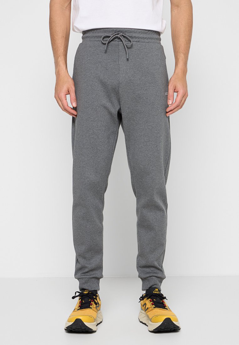 Pantaloni jogger grigi con vita regolabile, gambe affusolate e una texture morbida. Indossati con sneaker nere e gialle. Nessun motivo o logo visibile.