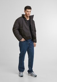 Geacă puffer neagră cu guler înalt, fermoar frontal și un design scurt. Asortată cu blugi din denim albastru și adidași gri. Simplă și modernă.