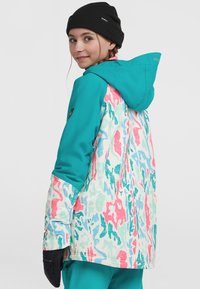Teal sneejakke med et multikulturelt abstrakt mønster i pink, blå og grøn. Har hætte og sorte handsker, generelt tekstureret finish.