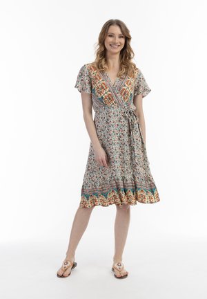 Das Wickelkleid hat ein florales Muster in Blau-, Orange- und Cremetönen; kurze Ärmel; fertiger Saum; das Modell trägt flache Sandalen.