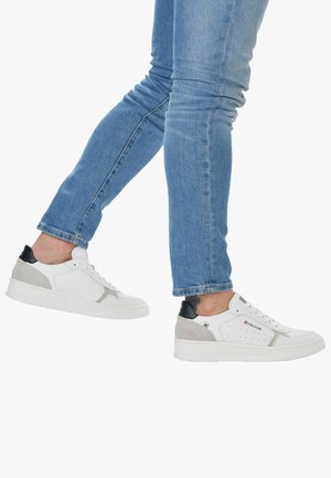 Weiße Sneakers mit grauen und schwarzen Akzenten, strukturiertem Leder und Wildledermaterialien, flacher Sohle und Belüftungsperforationen, getragen mit blauen Jeans.