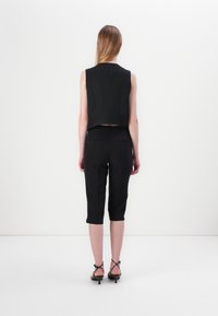 Crna bezrukavna crop majica sa strukturiranim dizajnom, uparen sa crnim hlačama do sredine lista. Odjevna kombinacija ima minimalne detalje i elegantne linije.