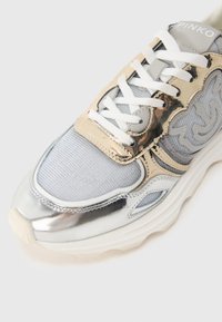 Αθλητικό παπούτσι σε ασημί και χρυσό με επάνω μέρος από δίχτυ, επενδεδυμένη γλώσσα και λευκά κορδόνια. Διακριτικές γυαλιστερές λεπτομέρειες και υφασμένο σχεδιασμό.