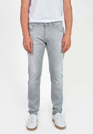 Jean en denim gris clair avec une coupe slim, présentant des effilochements subtils, un design à cinq poches, et associés à des baskets blanches.