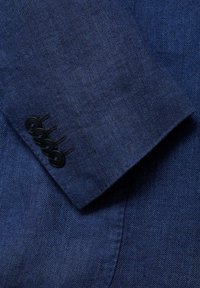 Gros plan sur la manche d'un blazer bleu avec quatre boutons noirs cousus en rangée près du poignet.