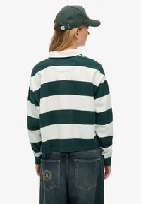 Grøn- og hvidstribet langærmet skjorte med krave, kombineret med denimbukser. Et grønt kasket fuldender outfittet, med synlige syninger bagpå.