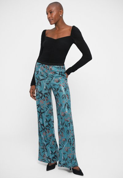 Melnā garo piedurknu krekls ar drapējuma detaļām, apvienots ar teal krāsas platām biksēm, kurām ir ziedu raksts sarkanos un melnos toņos. Komplektēts ar melnām kurpēm ar augstu papēdi.