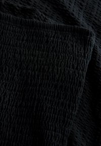 Gros plan d'un tissu noir texturé présentant un motif en relief quadrillé avec une partie pliée mettant en valeur l'épaisseur et les détails du matériau.