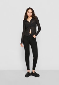 Top preto canelado de manga longa com botões e colarinho; combinado com jeans preto ajustados de cintura alta e mocassins pretos chunky.