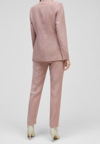 Rosa skräddarsydd kostym med en figursydd kavaj och raka byxor, tillverkad av slät textil. Har en enkel design och neutrala klackar.