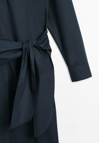 Vêtement bleu marine foncé à manches longues avec une large ceinture en tissu nouée en nœud à la taille, présenté sur un fond blanc uni.