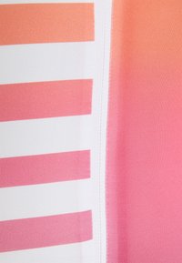 Gros plan d’un tissu avec une couture blanche verticale séparant des rayures roses et blanches à gauche d’un dégradé rose uni à droite.