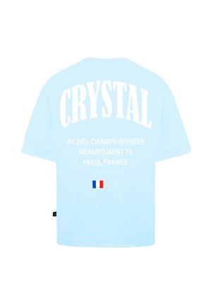 Maglietta azzurra a maniche corte con testo bianco che recita "CRYSTAL" e dettagli sulla località, con una piccola grafica della bandiera francese vicino al fondo.