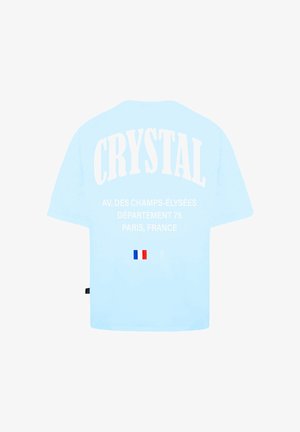 Světle modré tričko s krátkým rukávem, na kterém je bílé písmo "CRYSTAL" a informace o místě, spolu s malou francouzskou vlajkou graficky umístěnou blízko spodního okraje.