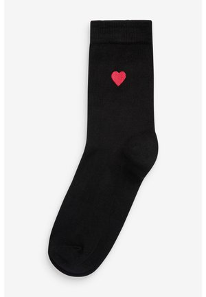 Črne bombažne nogavice z gladko teksturo, ki imajo majhen izvezen rdeč srček ob strani. Klasična zasnova do članka.