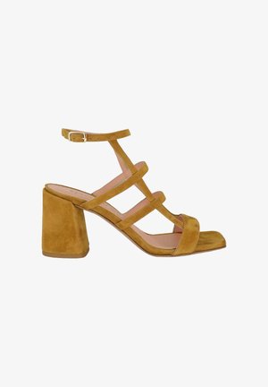 Sandalo con tacco a blocco in camoscio marrone con cinghia alla caviglia e tre sottili cinturini incrociati, punta aperta e tacco quadrato su sfondo bianco.