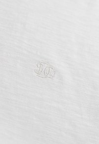 Close-up of white fabric with a subtle, raised embroidered logo consisting of intertwined letters "D" and "C".
