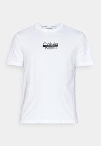Camiseta de algodón blanca con un logo negro de Calvin Klein centrado en el pecho. Diseño de mangas cortas y cuello redondo. Textura suave.
