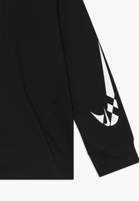 Maglia nera a maniche lunghe con una texture liscia, presenta un logo Nike bianco sulla manica sinistra e un orlo leggermente curvo in basso.
