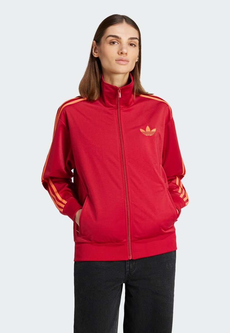 Rote Zip-Jacke aus glattem Stoff mit orangefarbenen Streifen an den Ärmeln und einem gestickten Logo auf der Brust. Verfügt über Seitentaschen.