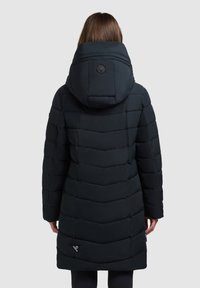 Fekete pufferceg kabát nagy kapucnival, csepp mintázatú varrással és logó címkével az alján. Simább, steppelt textúra.