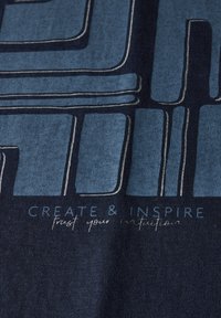 Un tissu bleu foncé avec une finition texturée présente de grandes formes graphiques bleu clair et un texte blanc indiquant "CRÉER & INSPIRER".