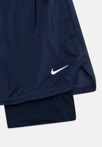 Väri merivoimien urheilushortsit, joissa on teksturoitu kangas ja valkoinen Nike-logo vasemmassa alakulmassa. Sisävuori on tumman sävyinen.