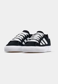 Black sneakers made of fabric with white laces, featuring three white stripes on the sides, and a white rubber sole with a textured bottom.