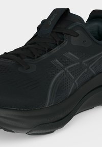 Μαύρο αθλητικό παπούτσι Asics με επάνω μέρος από δίχτυ, κορδόνια και επένδυση στον γιακά, που δείχνει υφασμένη πλευρική λογότυπο και παχύ μαλακό πέλμα.