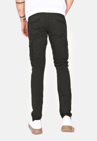 Pantaloni cargo neri con tasche laterali, dalla vestibilità slim e in misto cotone. Indossati con sneakers bianche, mostrano uno stile casual.