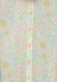 Blusa com estampa floral em cores pastel: flores cor-de-rosa, amarelas e azuis sobre um fundo verde-claro, com cinco botões cor-de-rosa na frente.