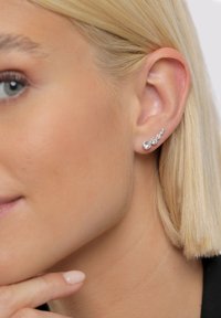 Sidabriniai auskarai su penkiais skirtingo dydžio skaidriais brangakmeniais, pasižymintys elegantišku dizainu, kuris atitinka ausies kreivę.