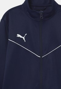 Marineblaue Sportjacke mit weißen Akzenten, durchgehendem Reißverschluss, hohem Kragen und weißem Puma-Logo auf der linken Brust. Glattes, strukturiertes Material.