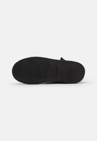 Suela de zapato negra con una superficie texturizada, que presenta un logo circular y ranuras horizontales para tracción. Diseño limpio y simple.