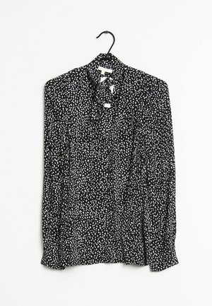 Black long-sleeve blouse with white irregular dot pattern, featuring a tie-neck detail, hanging on a black hanger against a white background.