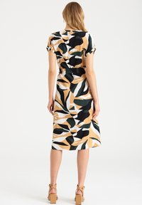 Klänning med korta ärmar i en beige, svart, vit och grön abstrakt bladdesign. Tyget verkar slätt, klänningen är knälång och har ett bälte i midjan.