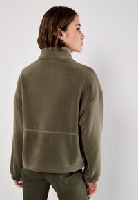 Olivengrøn fleecepullover med høj krave, afslappet pasform, sænkede skuldre og en glat tekstur. Har syningdetaljer henover ryggen.