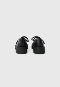 Scarpe in pelle nera con tacco a blocco basso e punta arrotondata. Presentano cinturini sottili e un design minimalista, con una texture liscia.