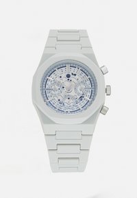 Montre octogonale blanche avec un cadran squelette transparent, présentant des accents argentés, un bracelet en caoutchouc et des repères horaires détaillés.
