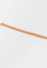 Nahaufnahme eines weißen, strukturierten Stoffes mit einer horizontal querliegenden, orangefarbenen Strickkordel in der Mitte.