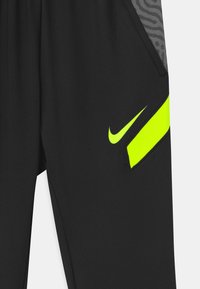 Schwarze Sporthose mit glatter Textur, die ein graues gemustertes Panel und ein leuchtend gelbes Nike-Logo sowie Akzente entlang der Seite aufweist.
