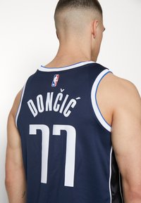 Marineblå basketballtrøje med hvid skrift, der viser "DONČIĆ" og nummer "77." Har en rund hals og kontraststikningsdetaljer.