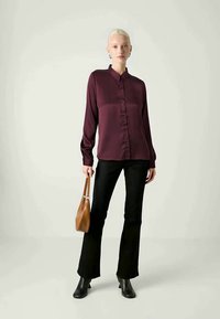 Burgundy button-up shirt with long sleeves, smooth texture, tailored fit, paired with flared black pants and a brown handbag. Black ankle boots.