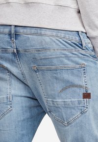 Ljusblå denimjeans har en klassisk passform, kontrasterande sömmar och två bakfickor med detaljer i läder.