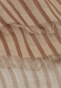 Tissu beige avec des bandes brunes alternées, présentant une texture subtile et des bords frangés. Matériau doux et léger.