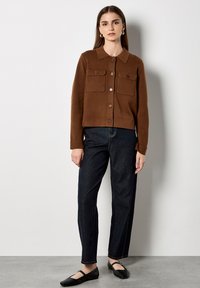 Bruine button-up cardigan met een kraag, voorzien van twee voorzakken en geribde manchetten, gecombineerd met donkere spijkerbroek en zwarte ballerina's.